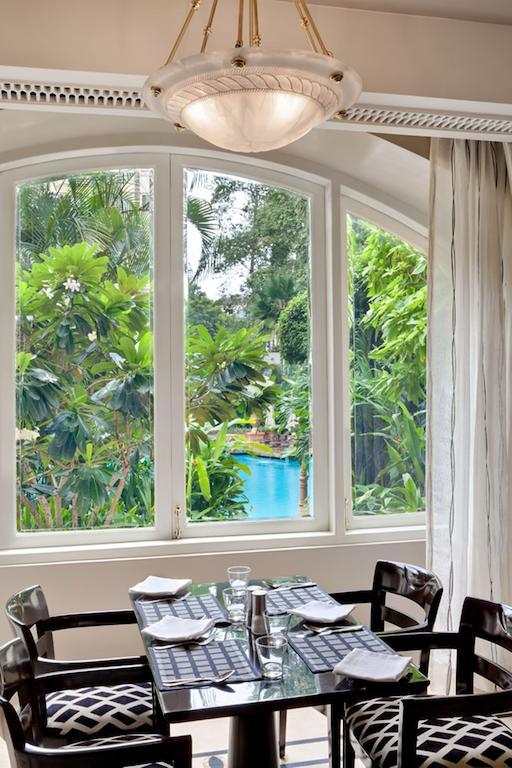 Hotel The Taj Mahal Tower, Bombay Esterno foto The photo shows a bright, airy indoor space with large windows framing a lush, green outdoor scene. Through the windows, you can see vibrant foliage, including various tropical plants and trees, creating a natural backdrop. In the distance, there is 
