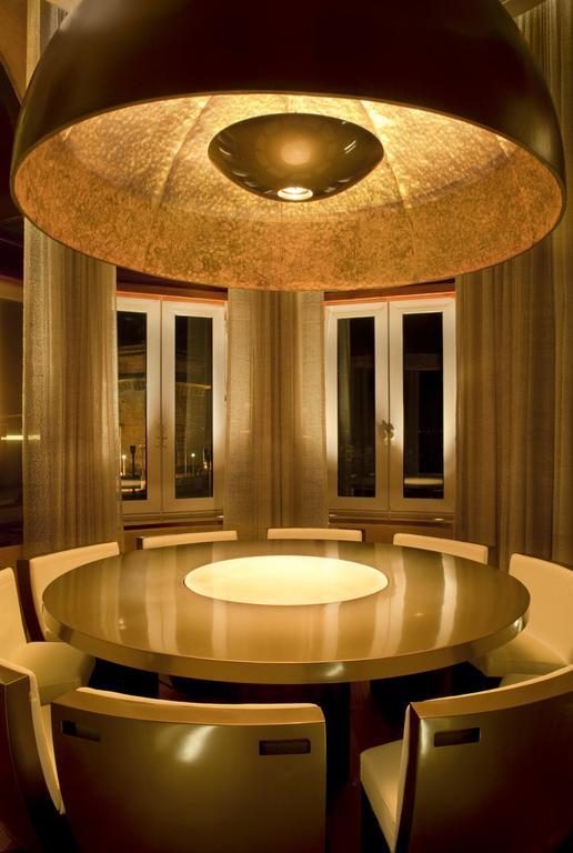 Hotel The Taj Mahal Tower, Bombay Esterno foto The photo shows a modern dining room with a round table at the center. The table has a glossy surface and features a circular illuminated section in the middle. Surrounding the table are sleek, contemporary chairs. The room has large windows dressed 