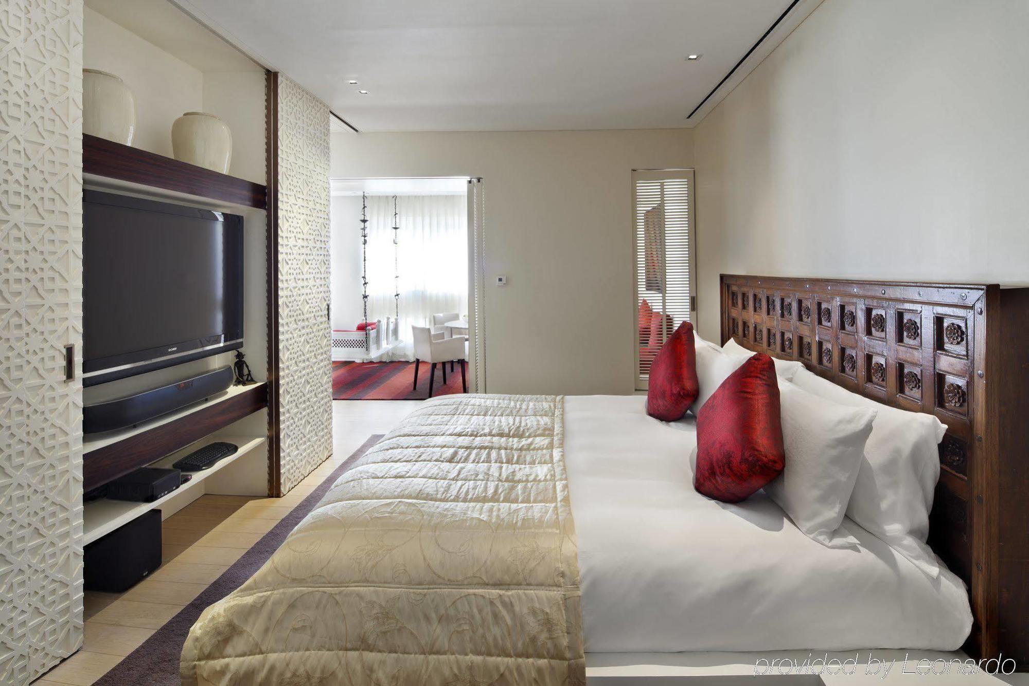 Hotel The Taj Mahal Tower, Bombay Esterno foto The photo depicts a modern hotel bedroom. The room features a large bed with white bedding and decorative red pillows. A beautifully carved wooden headboard adds an elegant touch. In the background, there is a flat-screen TV mounted on the wall, alon