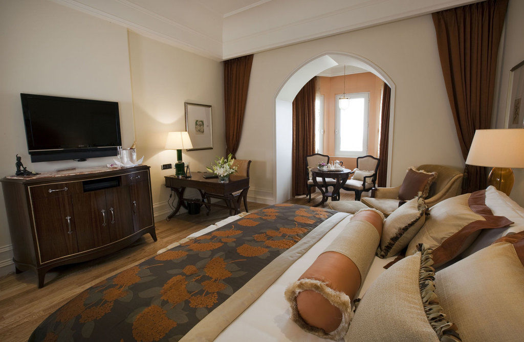 Hotel The Taj Mahal Tower, Bombay Esterno foto The photo shows a beautifully arranged hotel room featuring a king-size bed with decorative pillows and a stylish bedspread. Beside the bed is a modern wooden dresser with a flat-screen TV mounted on the wall. There is a cozy seating area with two ch